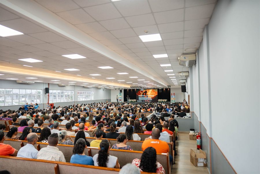 Large audience seated in a long conference hall facing a stage